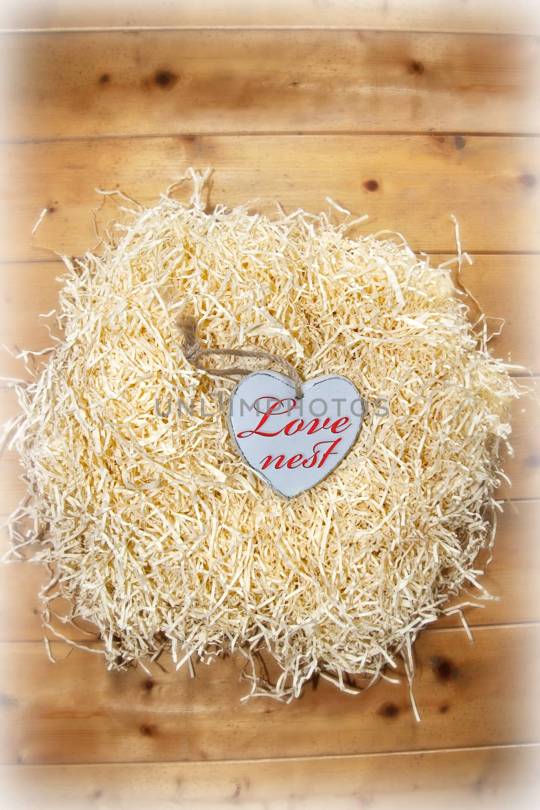 single wooden love heart in a love nest made of straw on floor boards