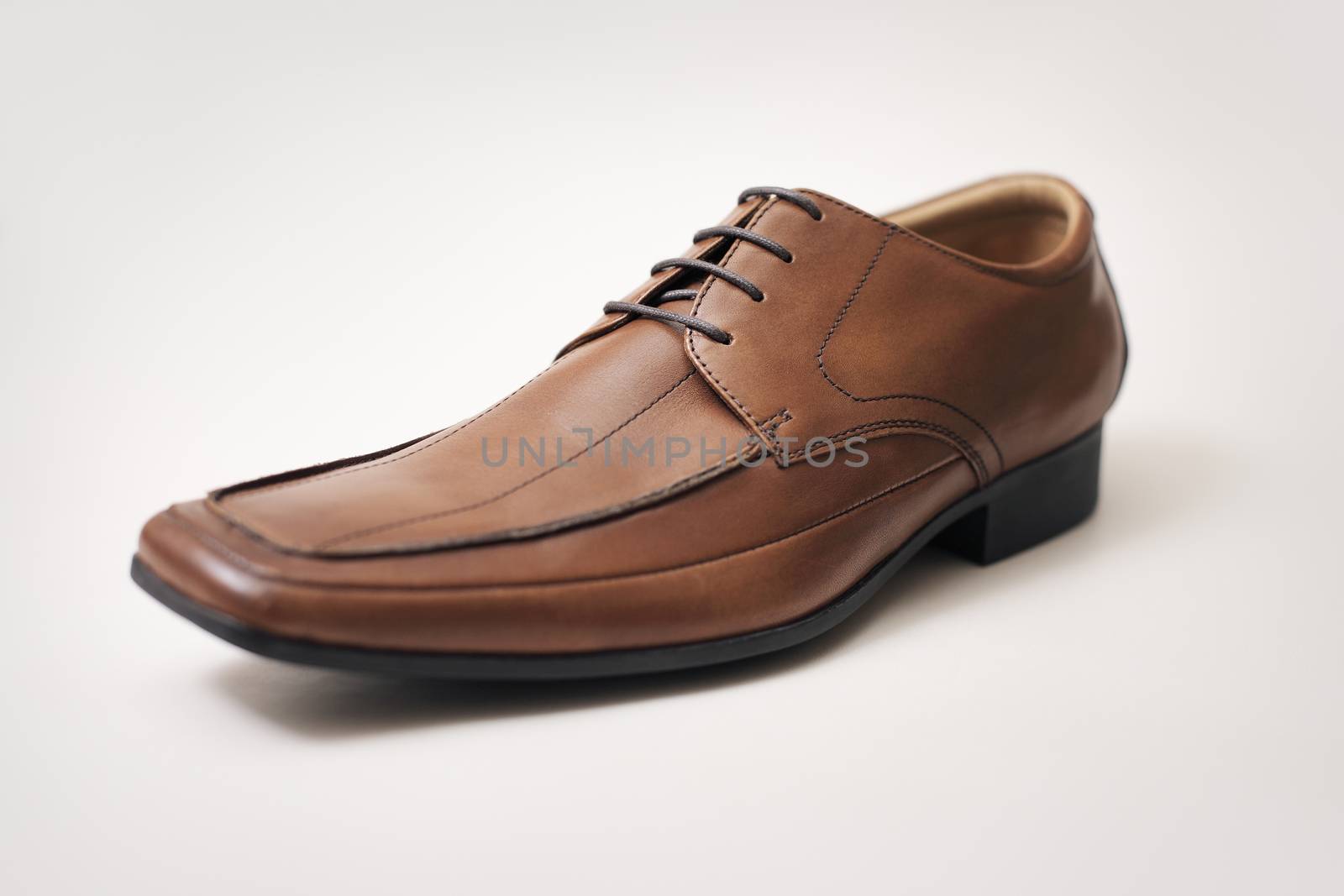 Men's brown leather shoe on light brown background. Very short depth-of-field.