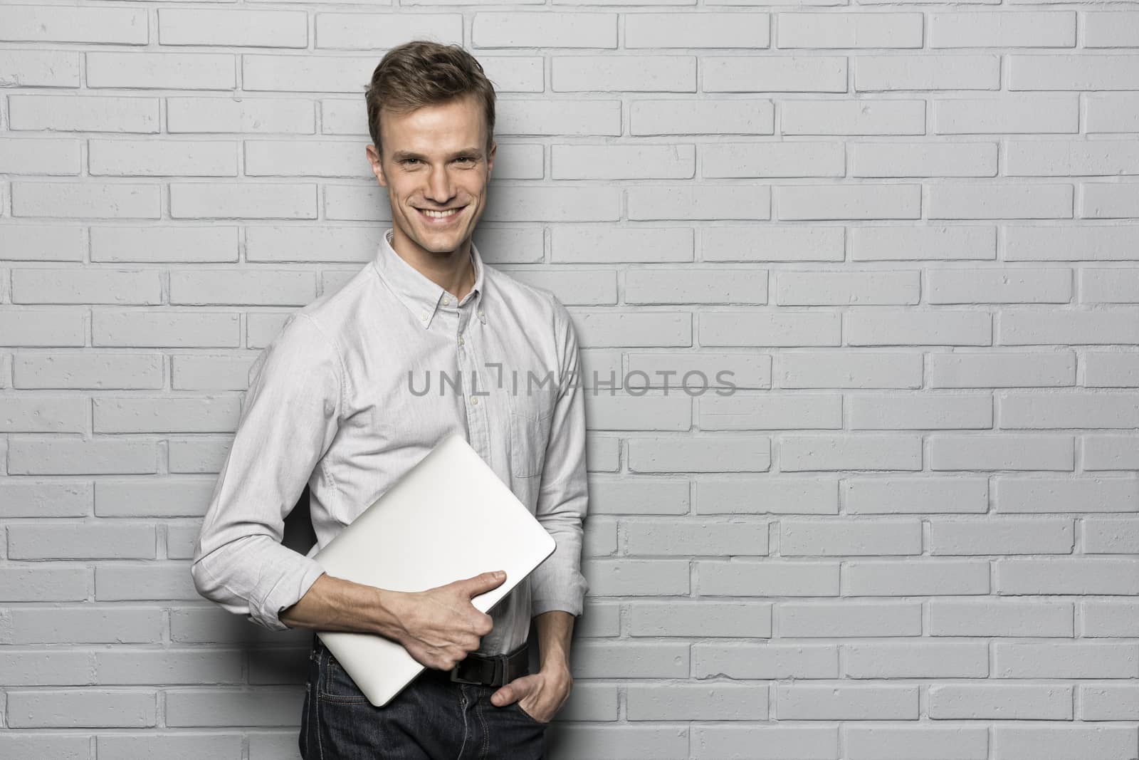Handsome man standing on Grey wall background,Whit Laptop by LDProd
