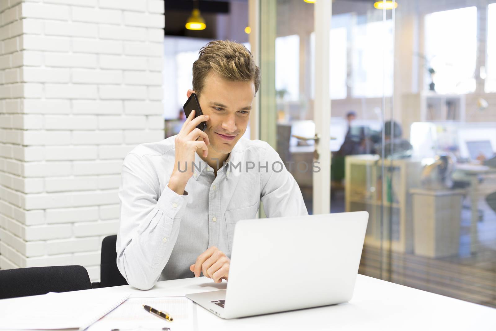 Young businessman on mobile phone in office by LDProd