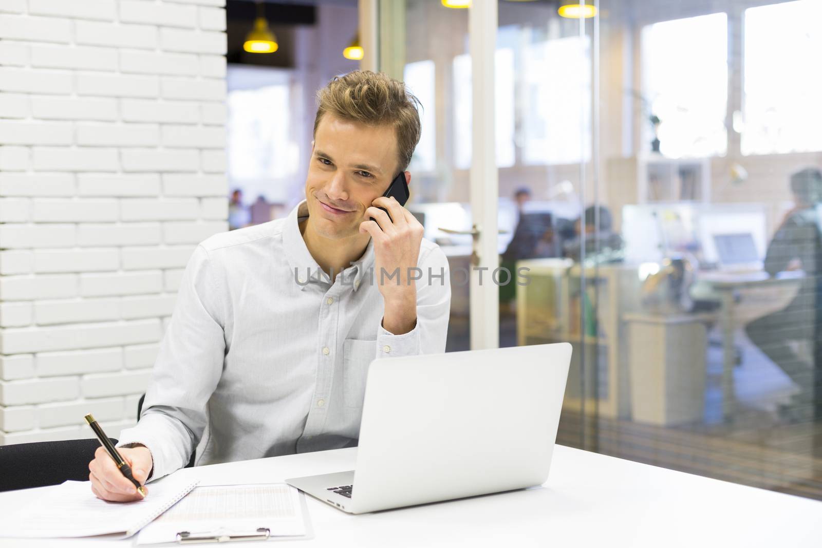 Young businessman on mobile phone in office by LDProd