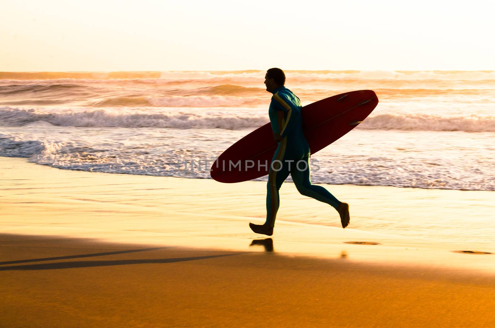 Surfer running on the beach with the waves at sunset in Portugal.