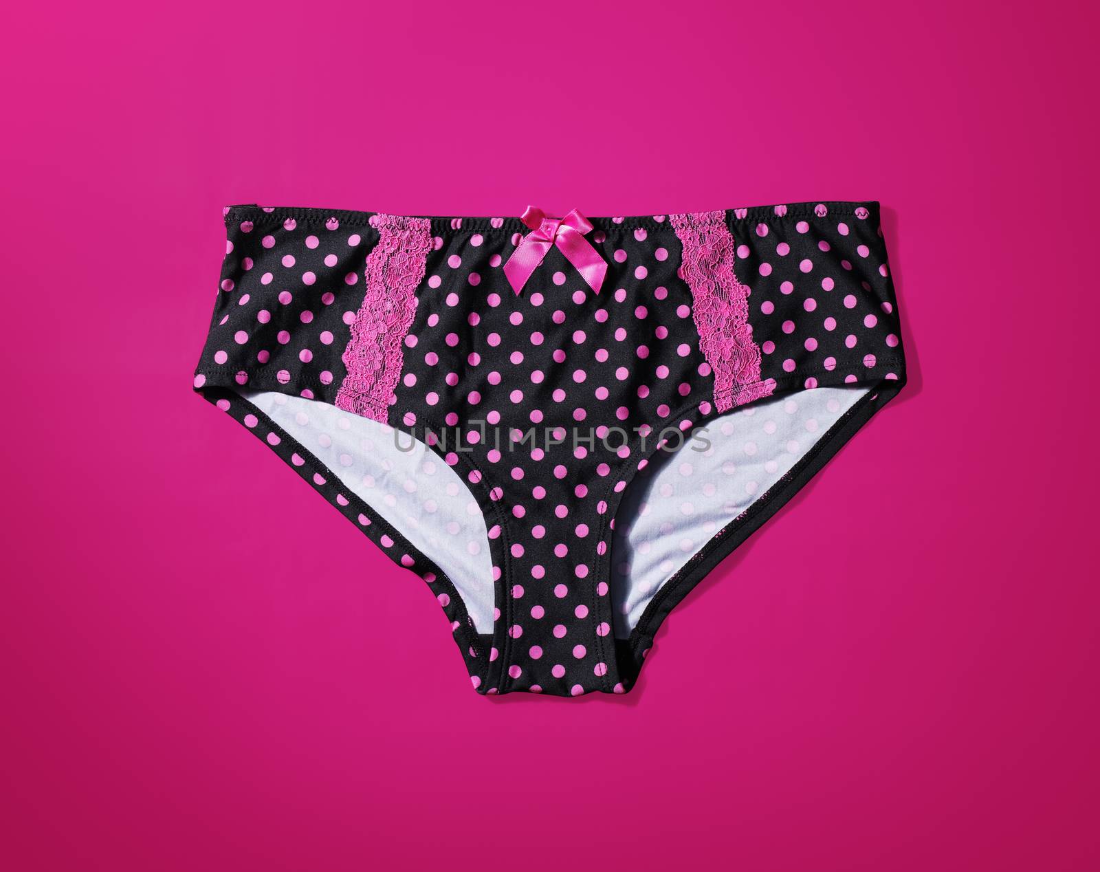 Women's black panties with pink polka dots on magenta background with natural shadows.