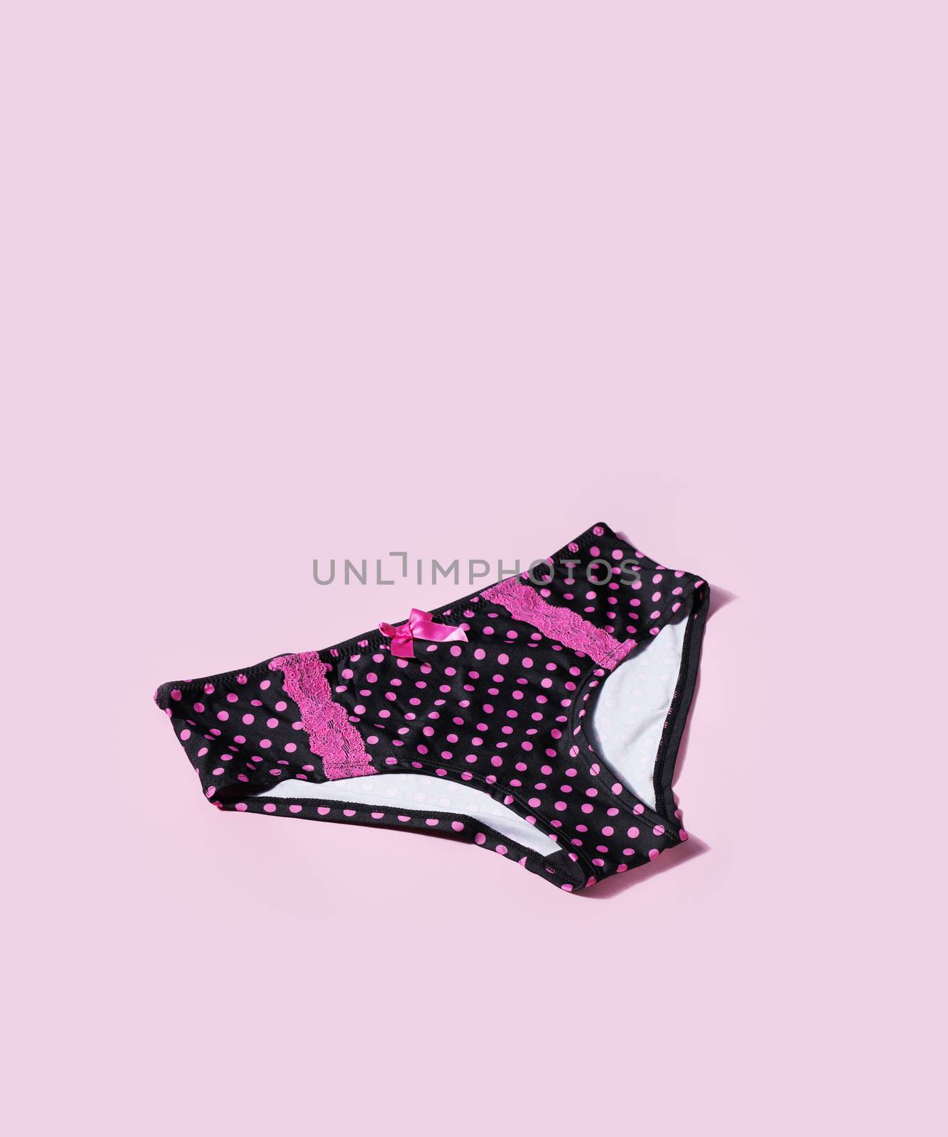 Women's black panties with pink polka dots on pink background with natural shadows.