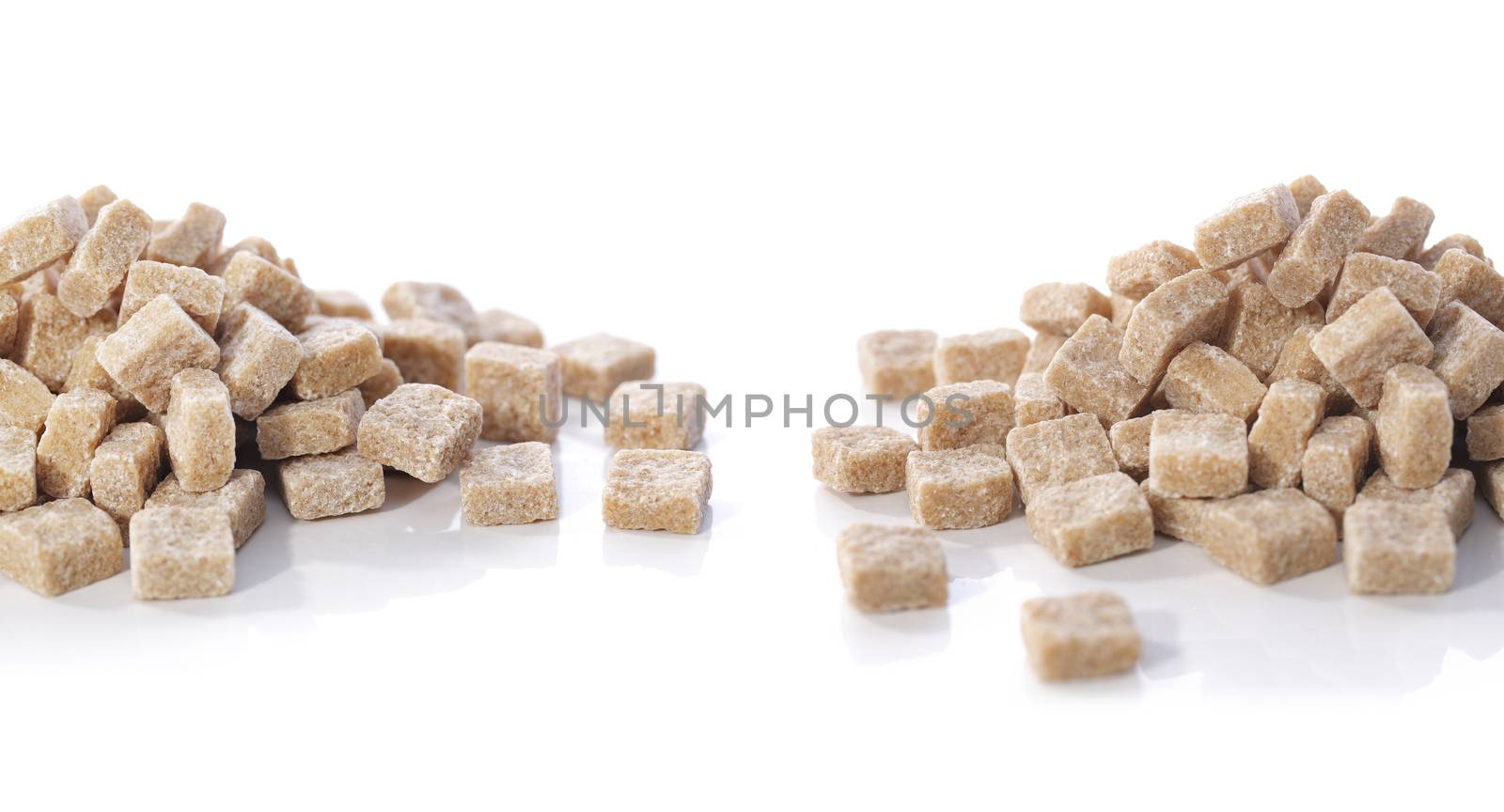 Two heaps of natural brown sugar cubes on white reflecting background