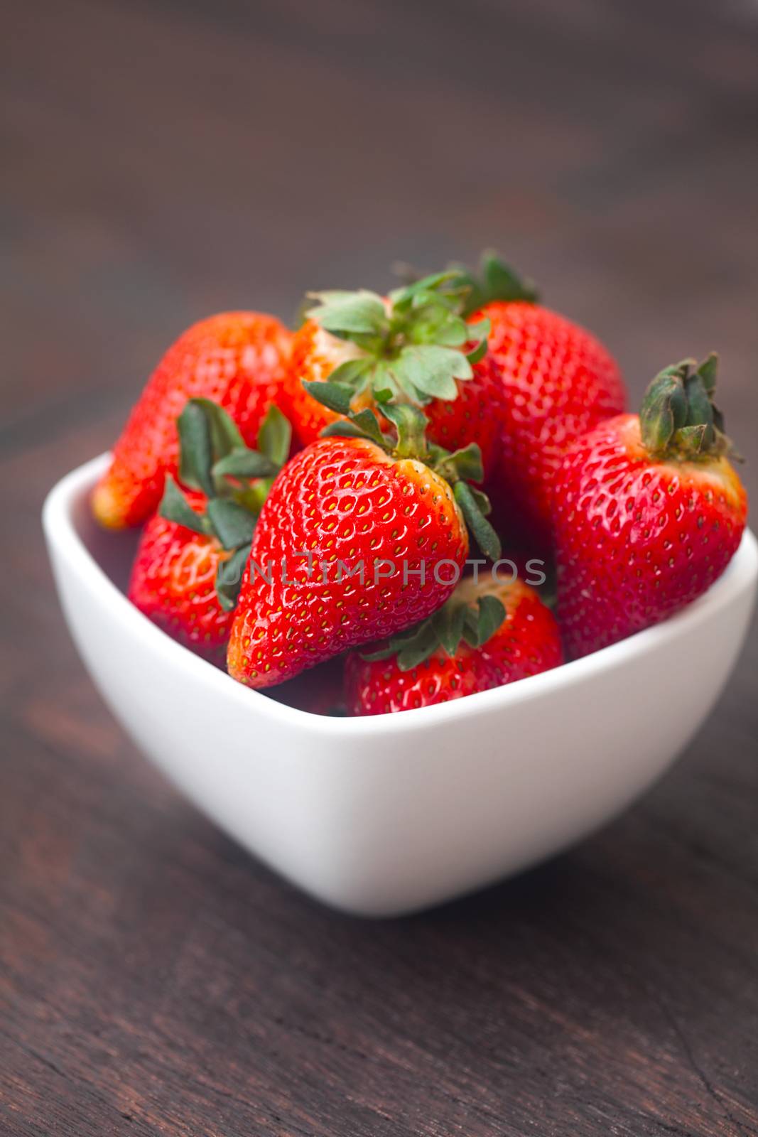 red juicy strawberry in a bowl on a wooden surface