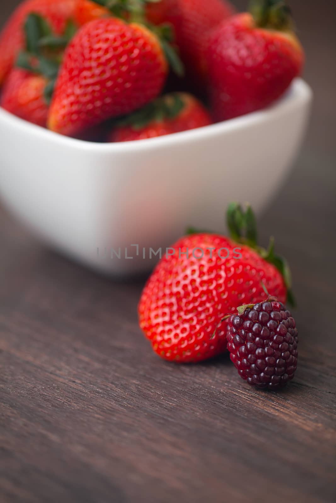 red juicy strawberry  in a bowl and blackberry on a wooden surface
