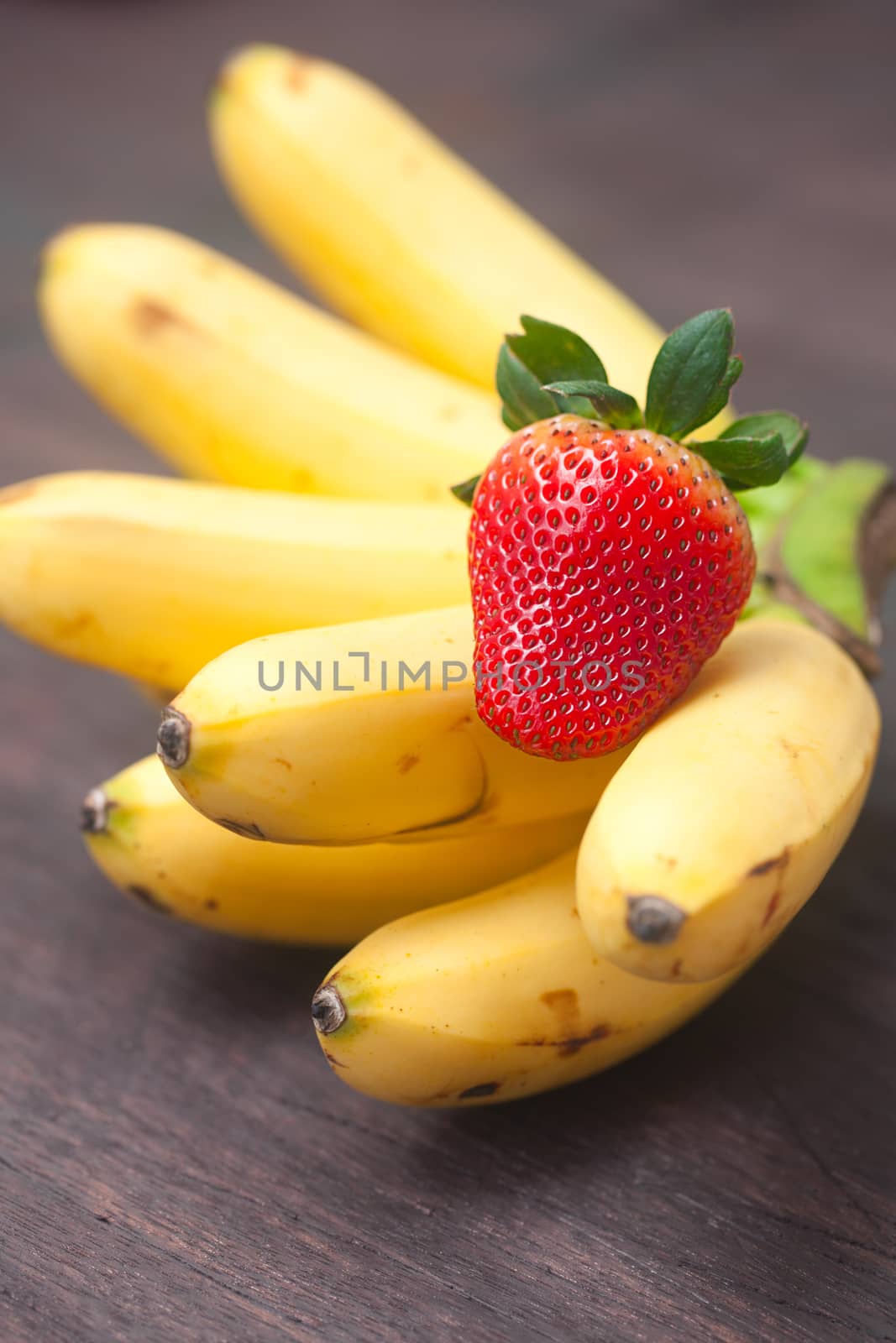 bunch of bananas anf strawberry on a wooden surface by jannyjus