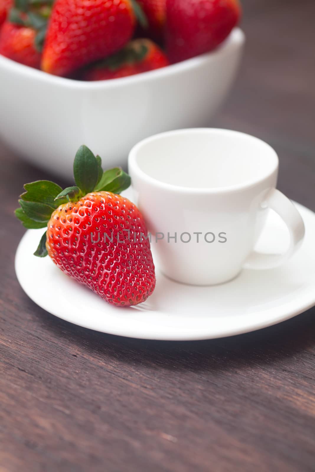 red juicy strawberry in a bowl and cup on a wooden surface