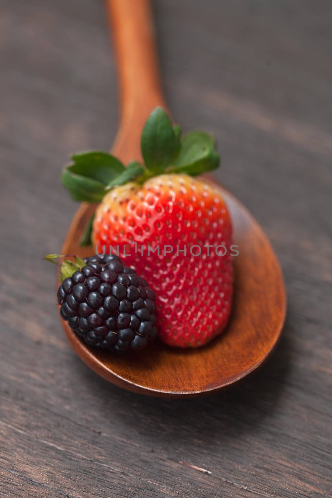 wooden spoon with strawberry and blackberry on a wooden surface by jannyjus