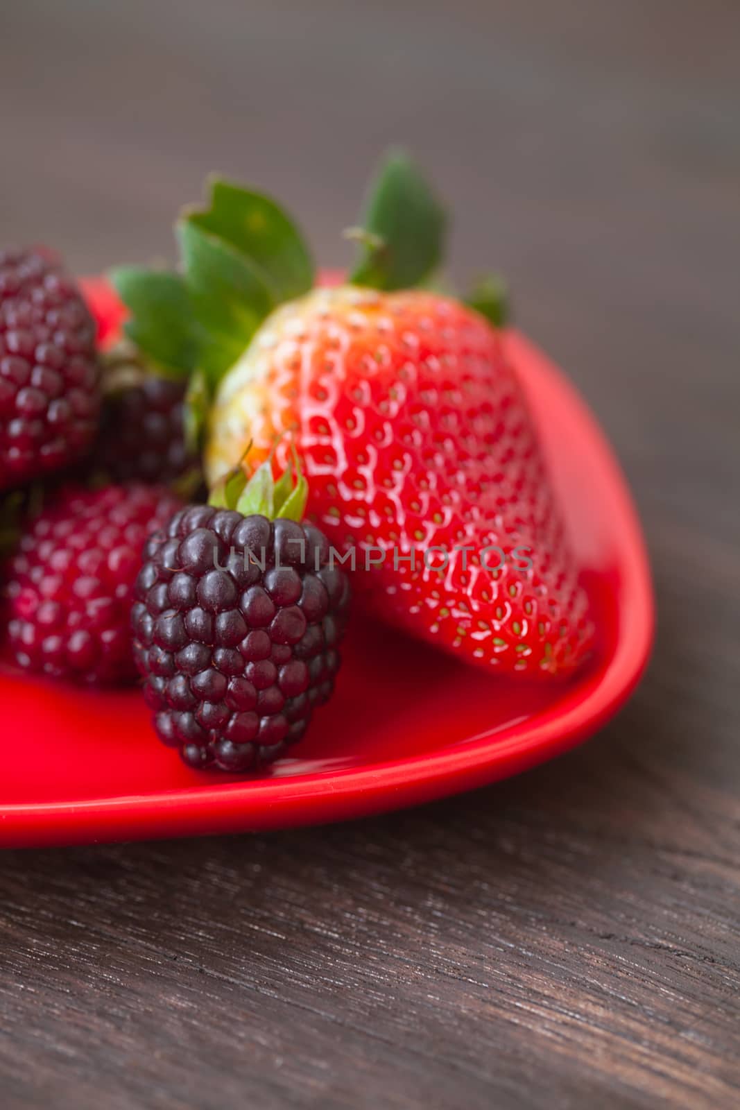 red juicy strawberry and blackberry in red plate on a wooden surface