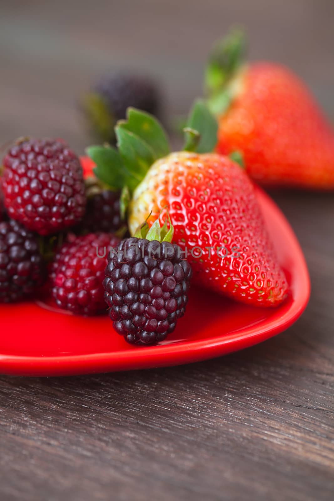 red juicy strawberry and blackberry in red plate on a wooden surface