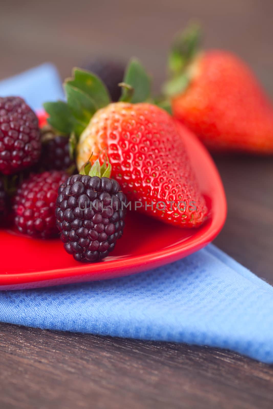 red juicy strawberry and blackberry in red plate on a wooden surface