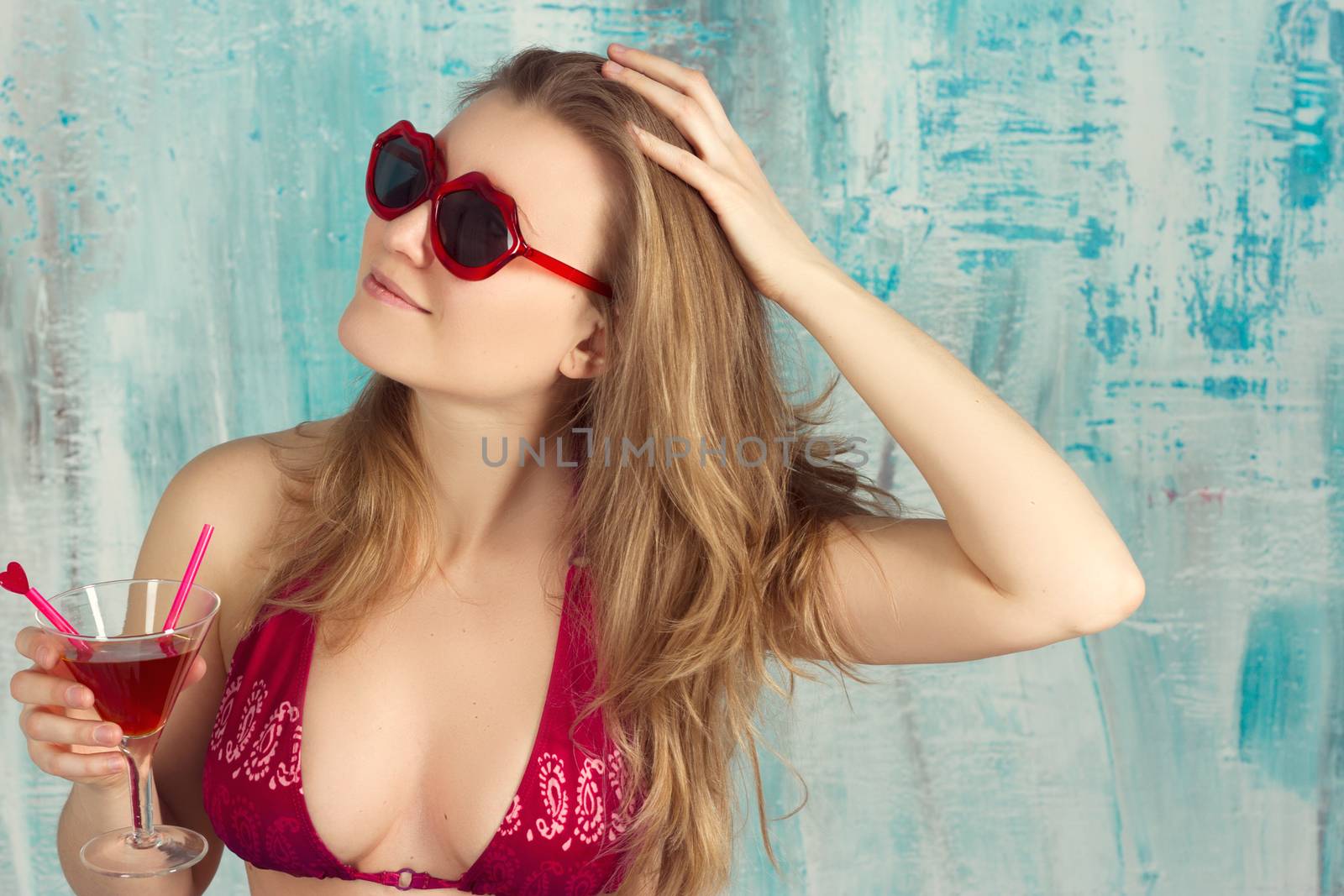 Beautiful girl drinking a cocktail against blue background.