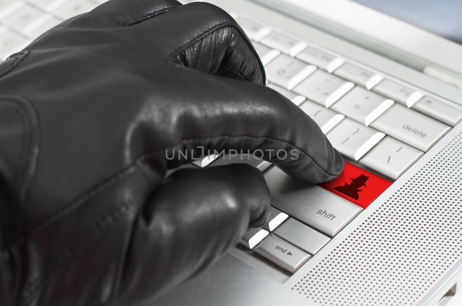 Online spy ware concept with hand wearing black leather glove pressing enter key on metallic laptop keyboard