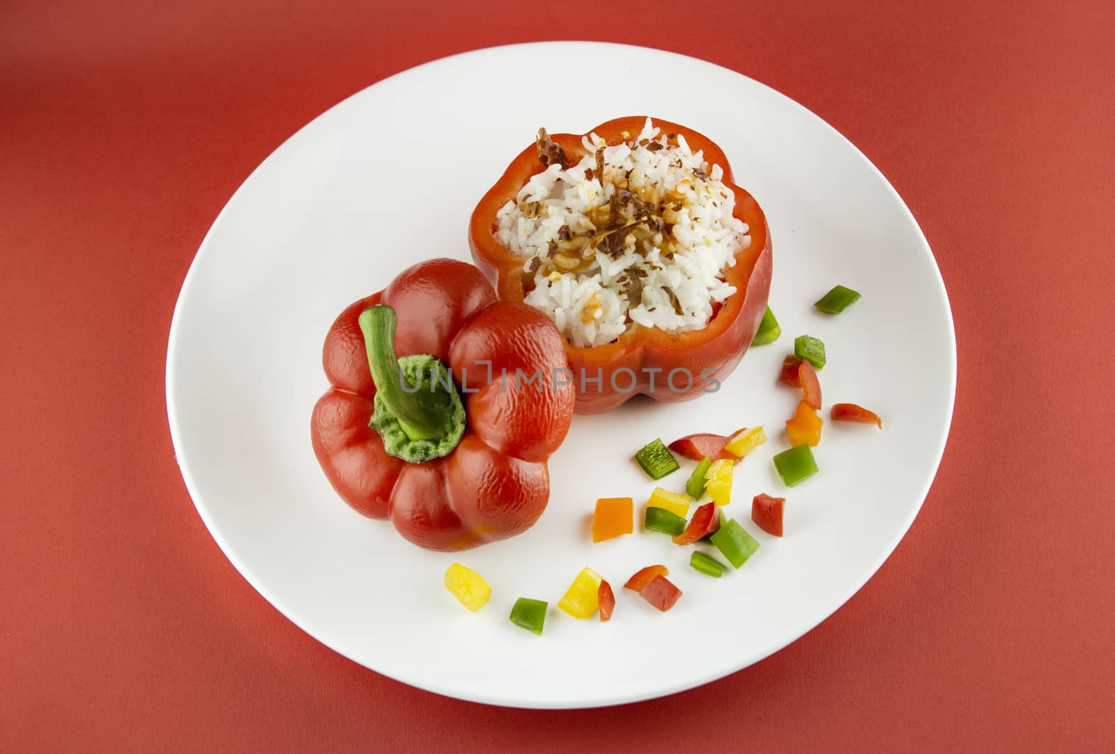 Stuffed red pepper in a dish on red background .
