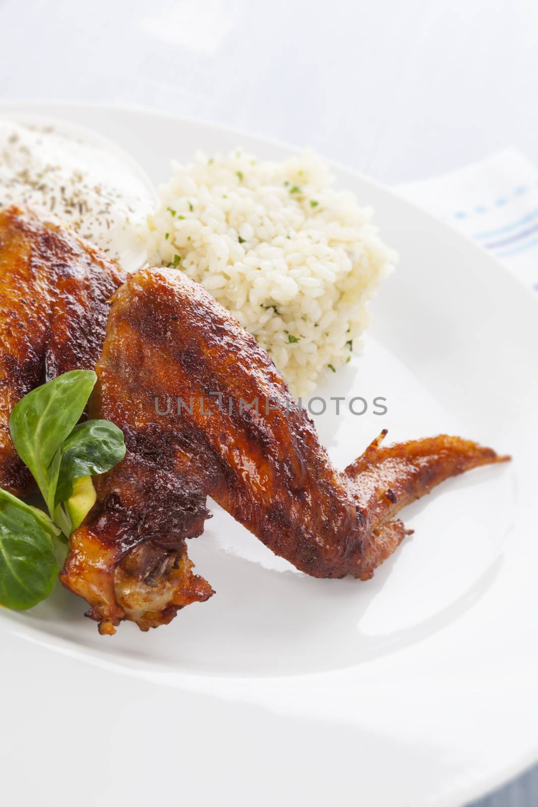 Barbeque chicken wing with rice, salad and dressing on white plate on bright background. Culinary chicken meat eating. 