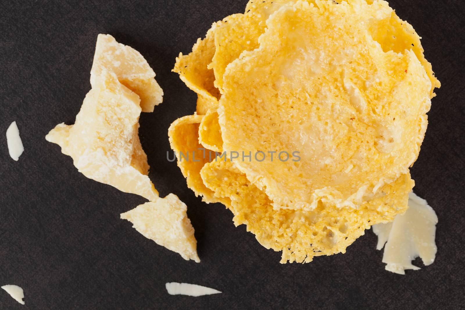 Parmigiano pieces and parmigiano basket on black background, top view. Culinary cheese eating.