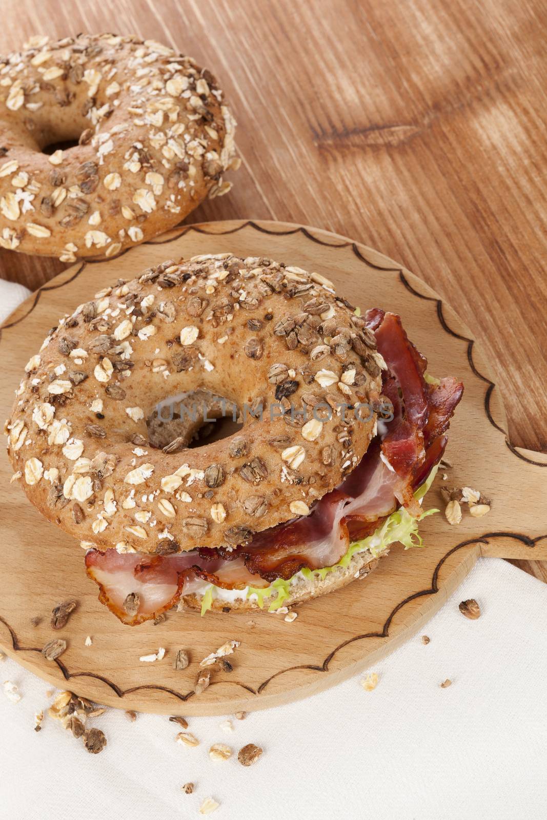 Delicious bagel eating. Whole grain bagel with bacon on wooden background. 