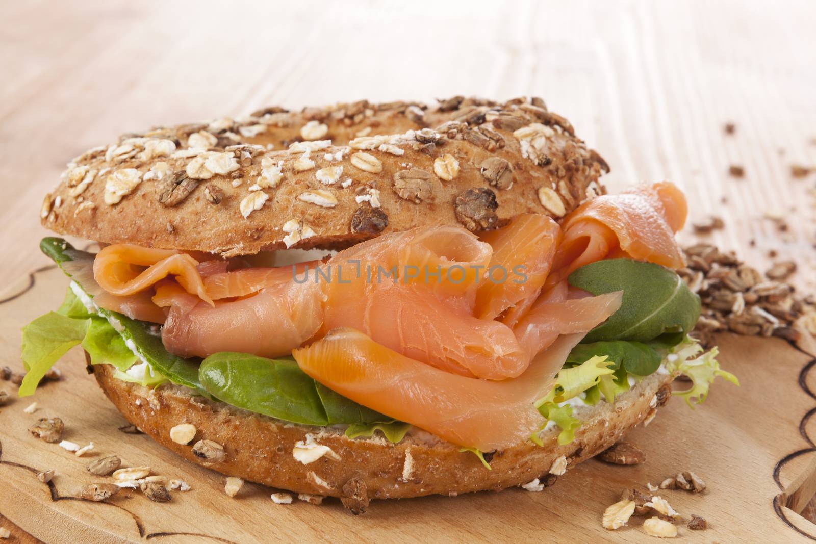 Whole grain bagel with smoked salmon on wooden background. Culinary healthy bagel eating.