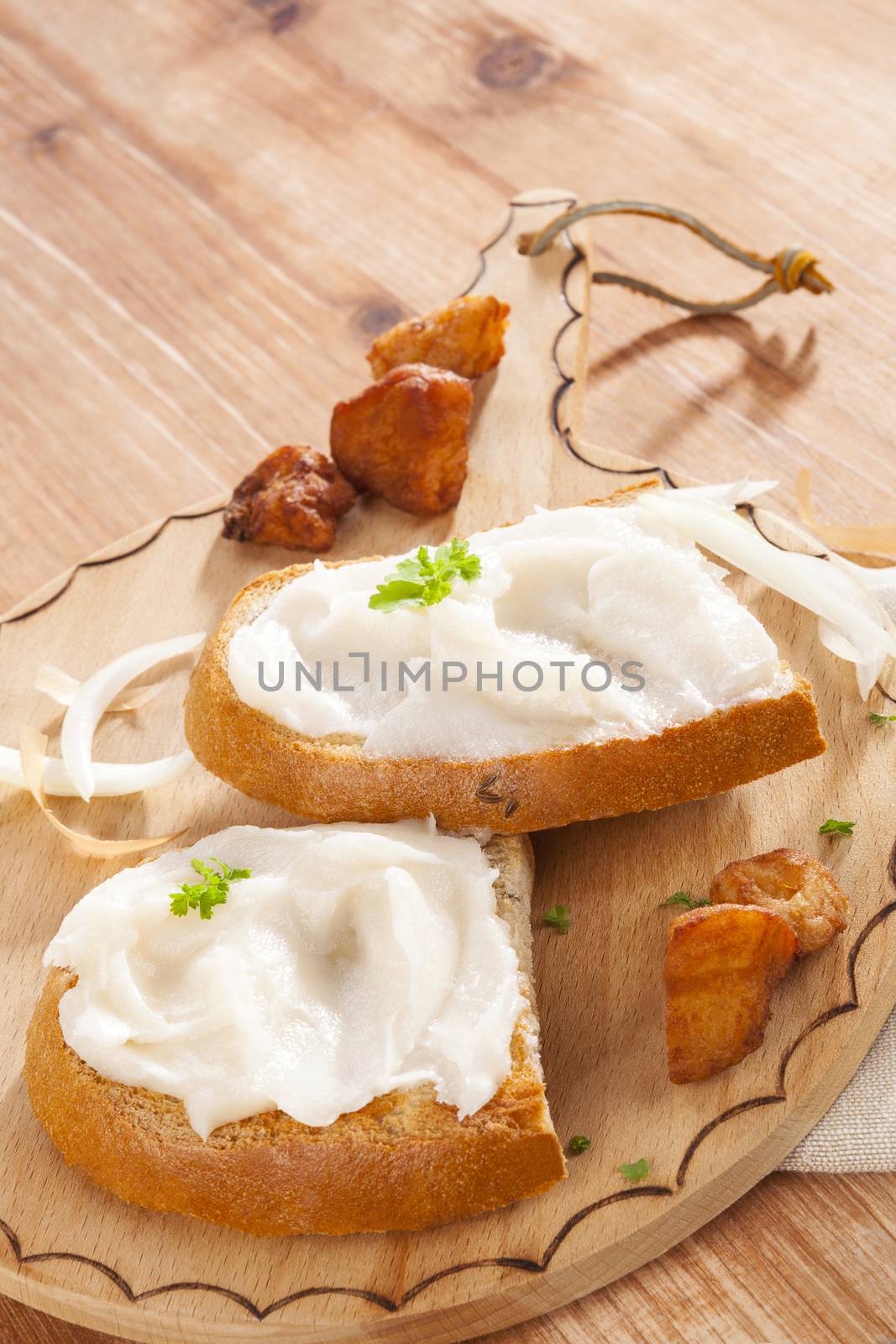 Bread slice with lard and cracklings on vintage wooden chopping board on wooden background. Traditional eating. 