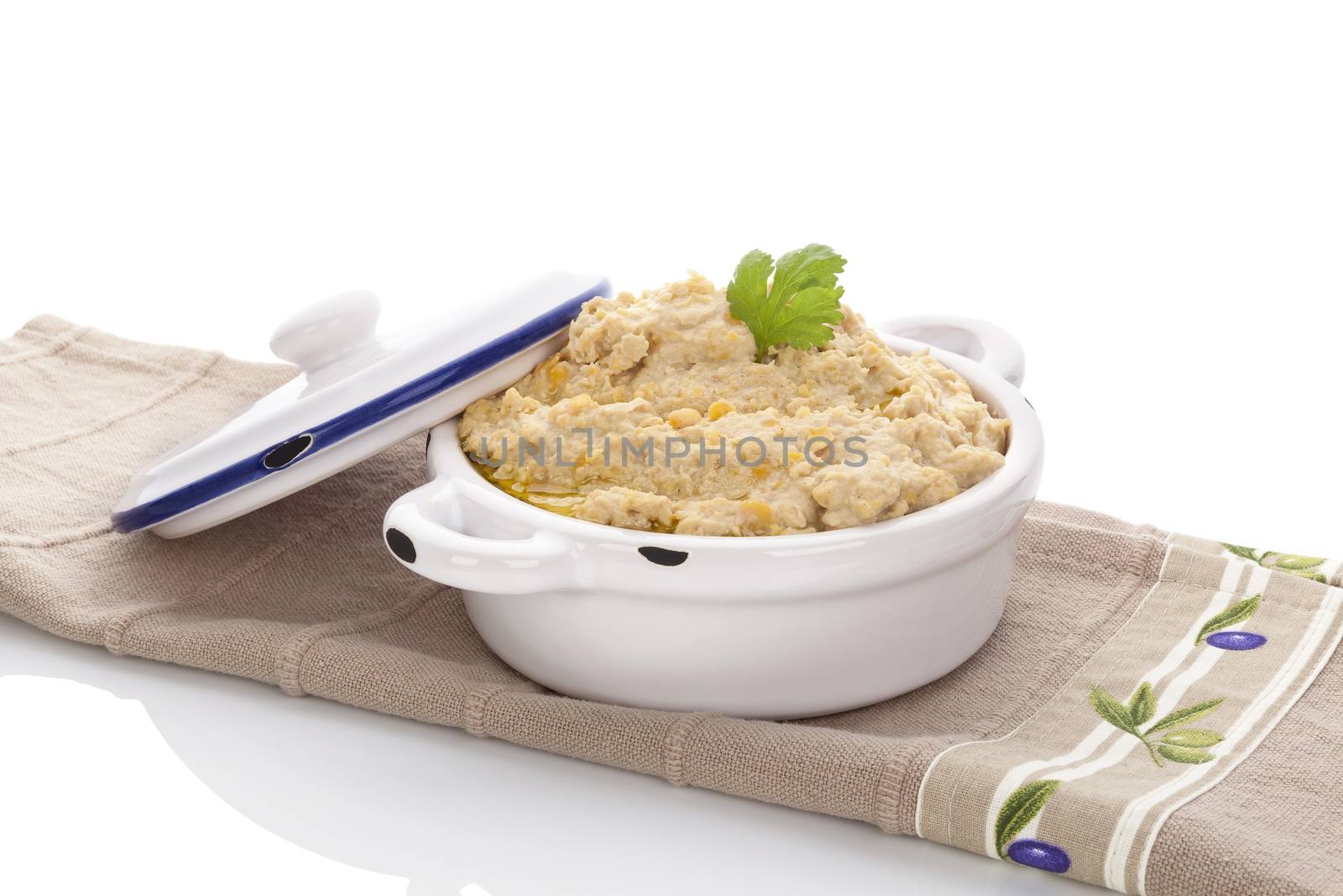 Delicious hummus in ceramic pot on brown table cloth isolated on white background. Traditional eastern eating.