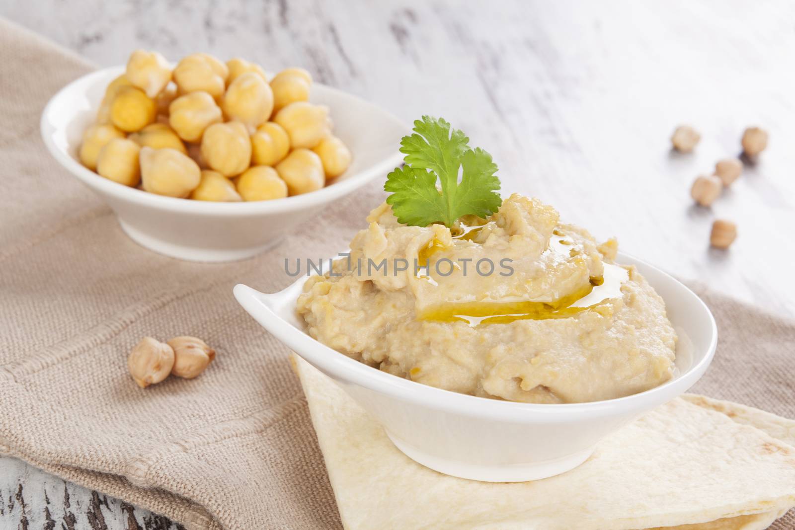 Delicious hummus and cooked chickpeas in bowl on white wooden background. Culinary hummus eating, mediterranean rustic style.