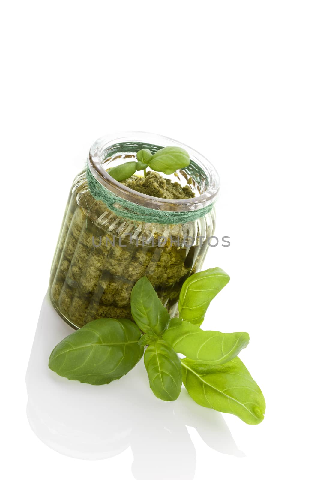 Green basil pesto in glass jar isolated on white background. Healthy vegetarian eating.