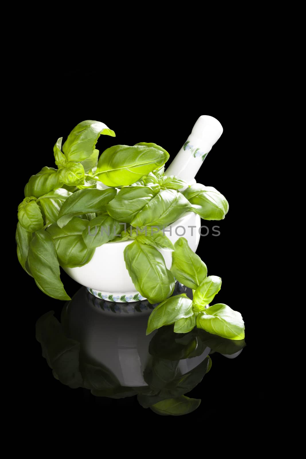 Fresh basil leaves in mortar and pestle isolated on black background. Aromatic culinary cooking herbs.