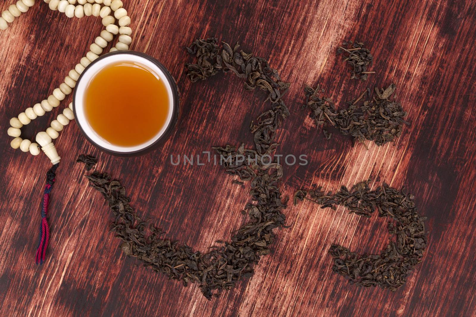 Cup of tea, dry tea leaves forming ohm symbol and buddhist necklace. Traditional tea drinking.