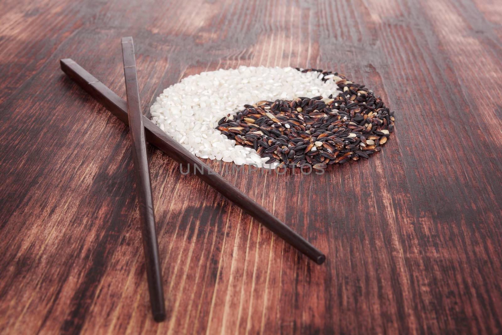 White and purple rice forming a Yin yang symbol with chopsticks on dark wooden background. Traditional chinese eating and culture.