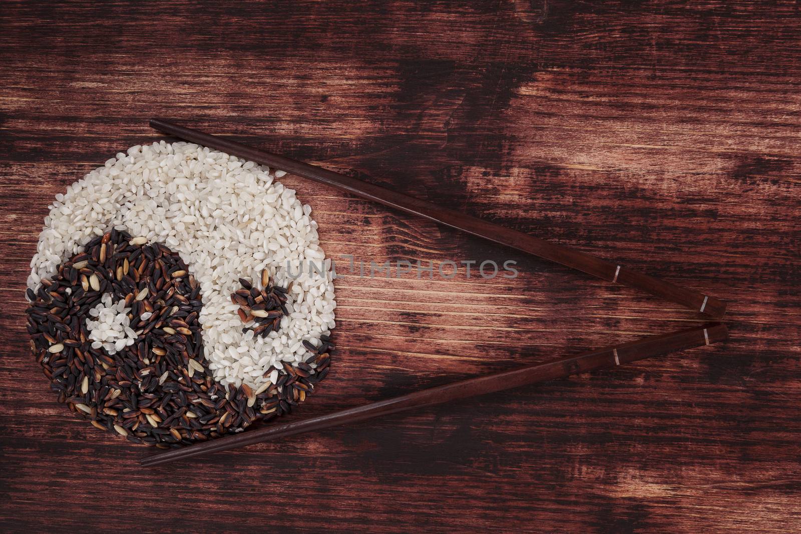White and wild rice forming a yin yang symbol with chopsticks on dark wooden background. Top view.