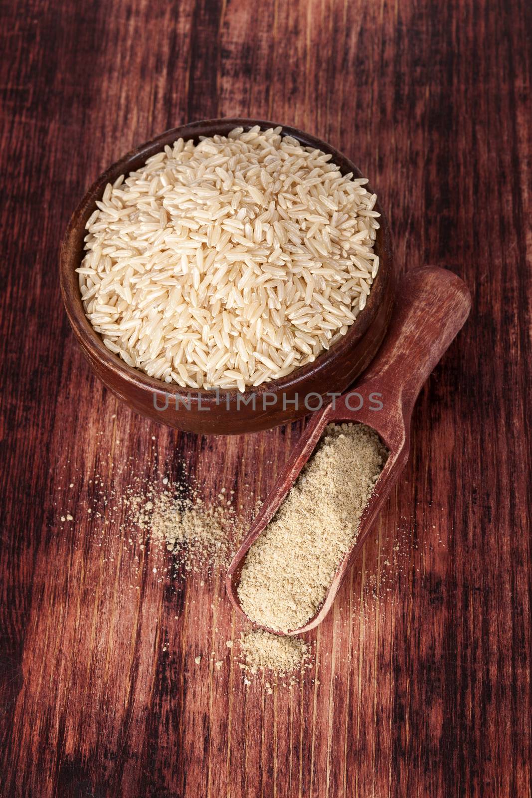 Rice in round wooden bowl with dietary rice fiber on wooden spoon on dark brown wooden background, top view. Healthy eating concept.