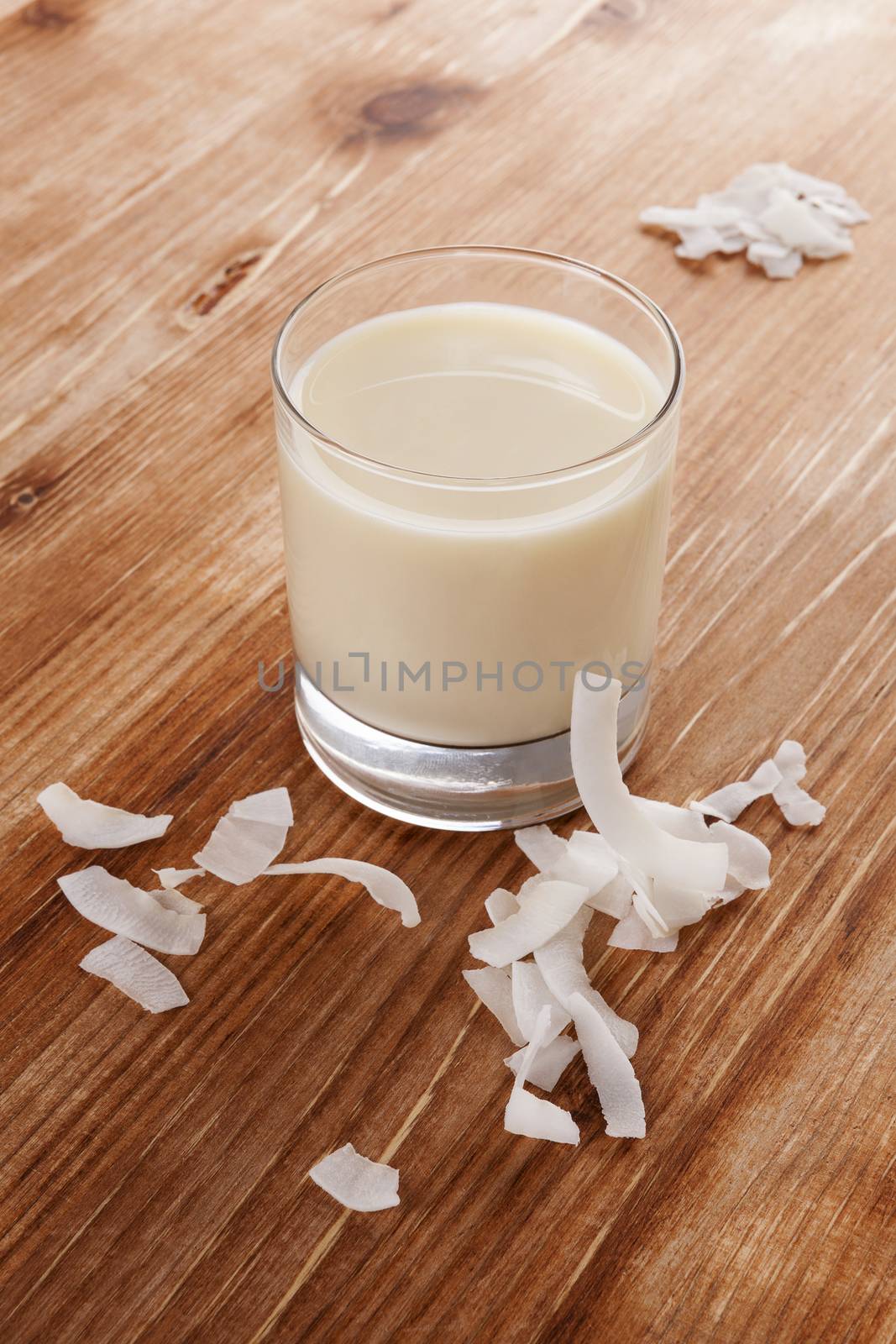 Glass of organic coconut milk with coconut flakes isolated on wooden background. Healthy vegan eating.
