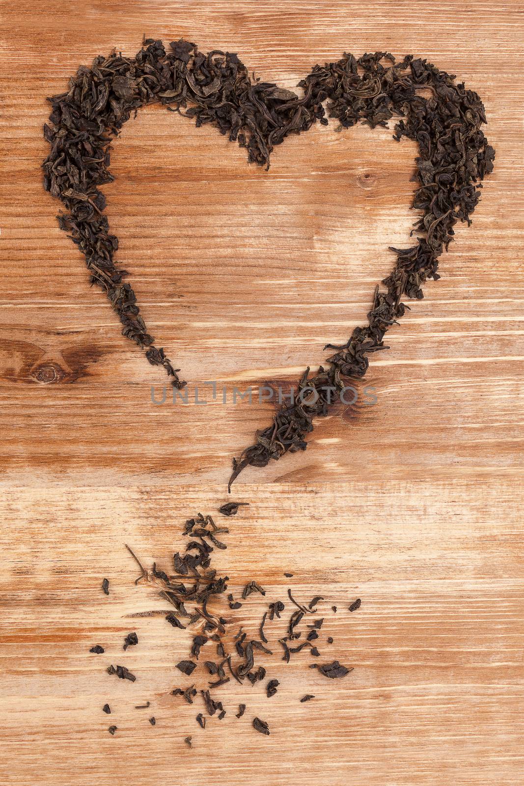 Organic dried green tea leaves in heart shape on wooden background. Traditional oriental beverage. 
