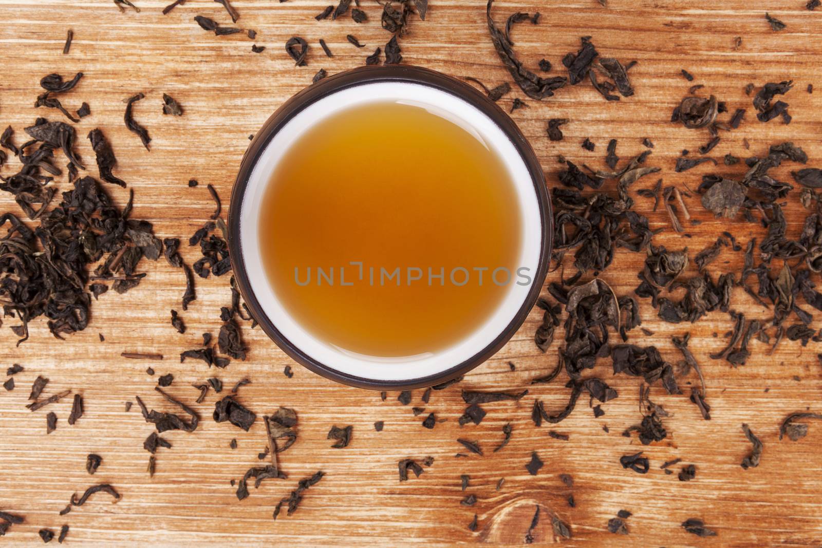 Mug of hot delicious green tea surrounded with dried leaves on wooden background. Delicious oriental beverage.  
