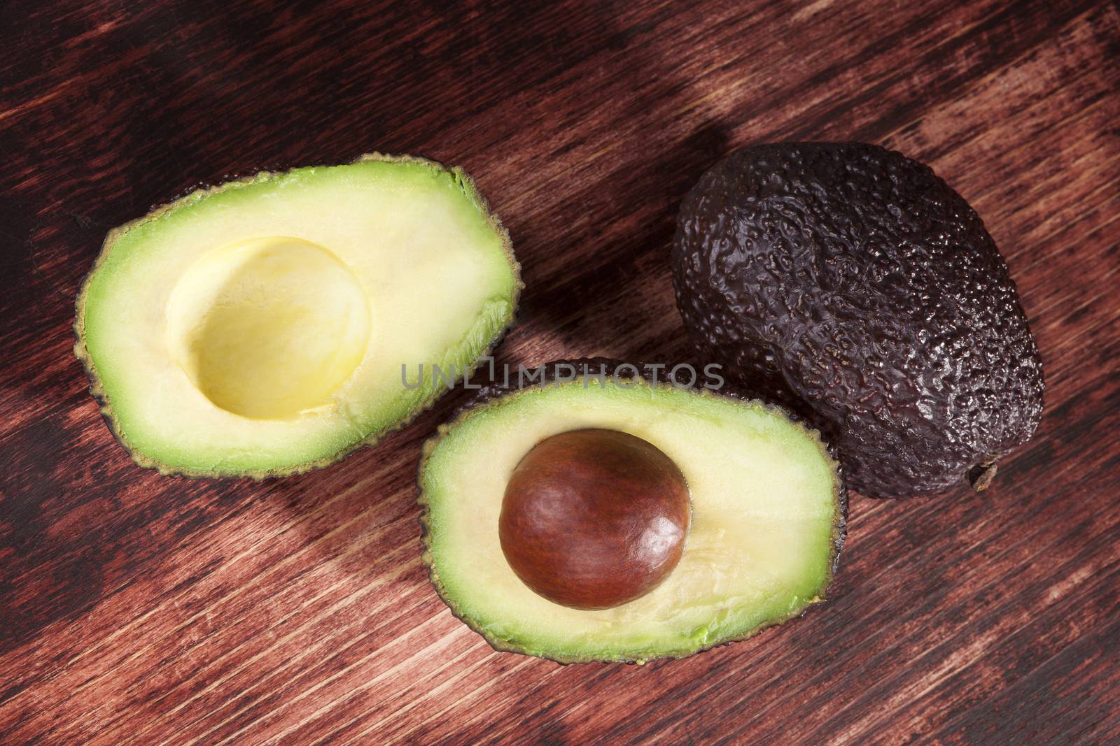 Delicious fresh ripe avocado cross section on brown wooden background, top view. Healthy fresh fruit eating.