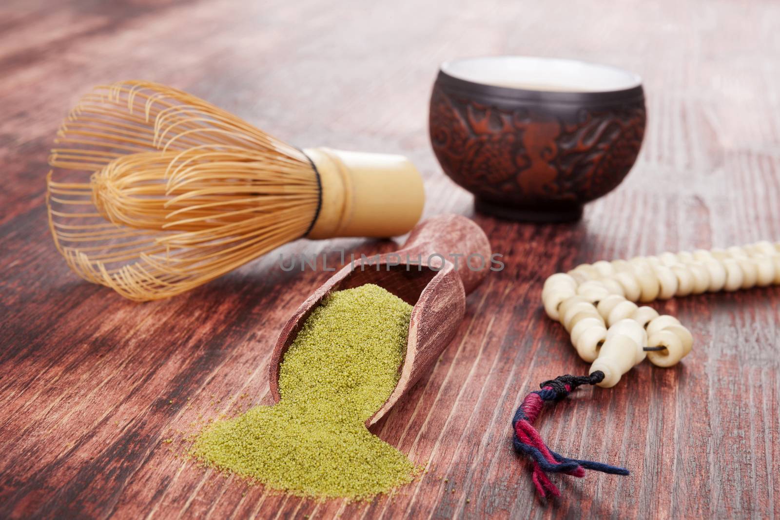 Traditional tea ceremony. Powdered green tea matcha, hot tea in ceramic cup, bamboo chasen and buddhist necklace on brown wooden background.