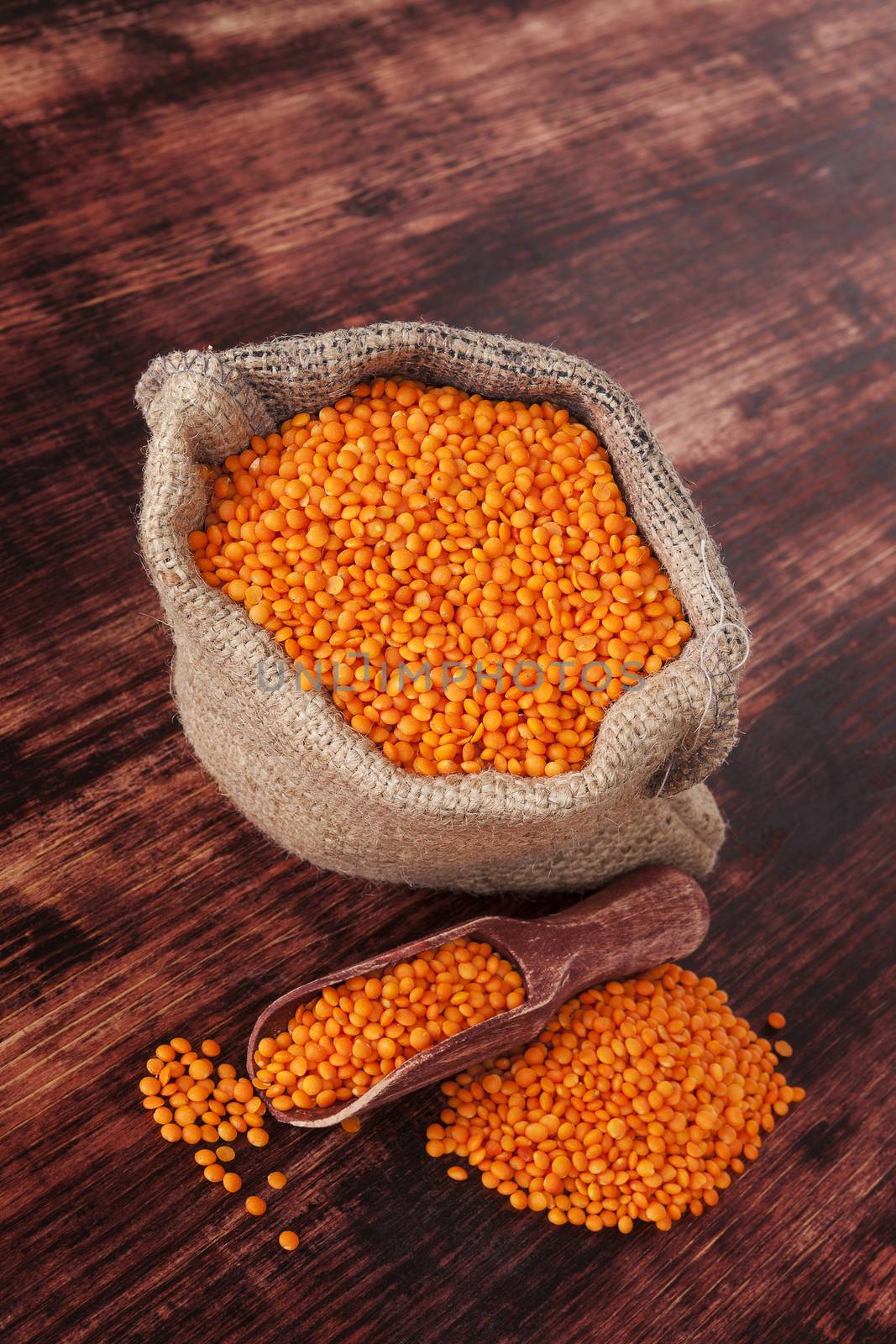 Red lentils in burlap sack with wooden spoon on dark wooden background. Healthy cooking.