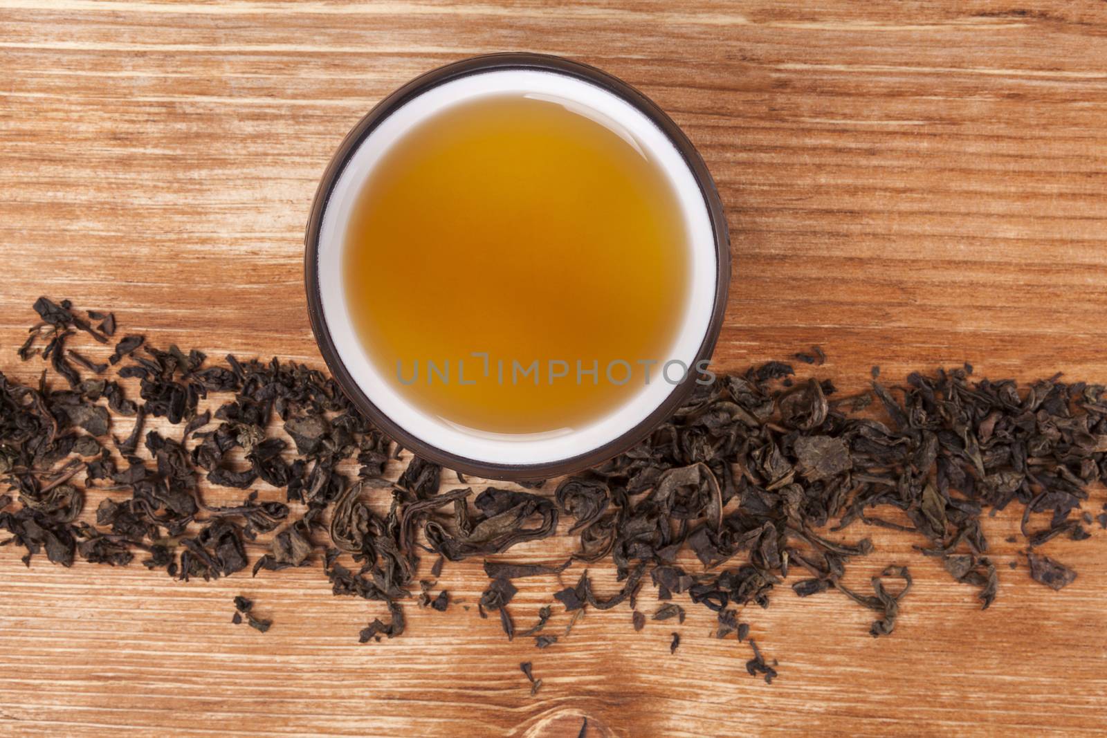 Dry tea leaves and dry green tea in cup on brown wooden background, top view. Healthy alternative medicine. Traditional tea drinking.