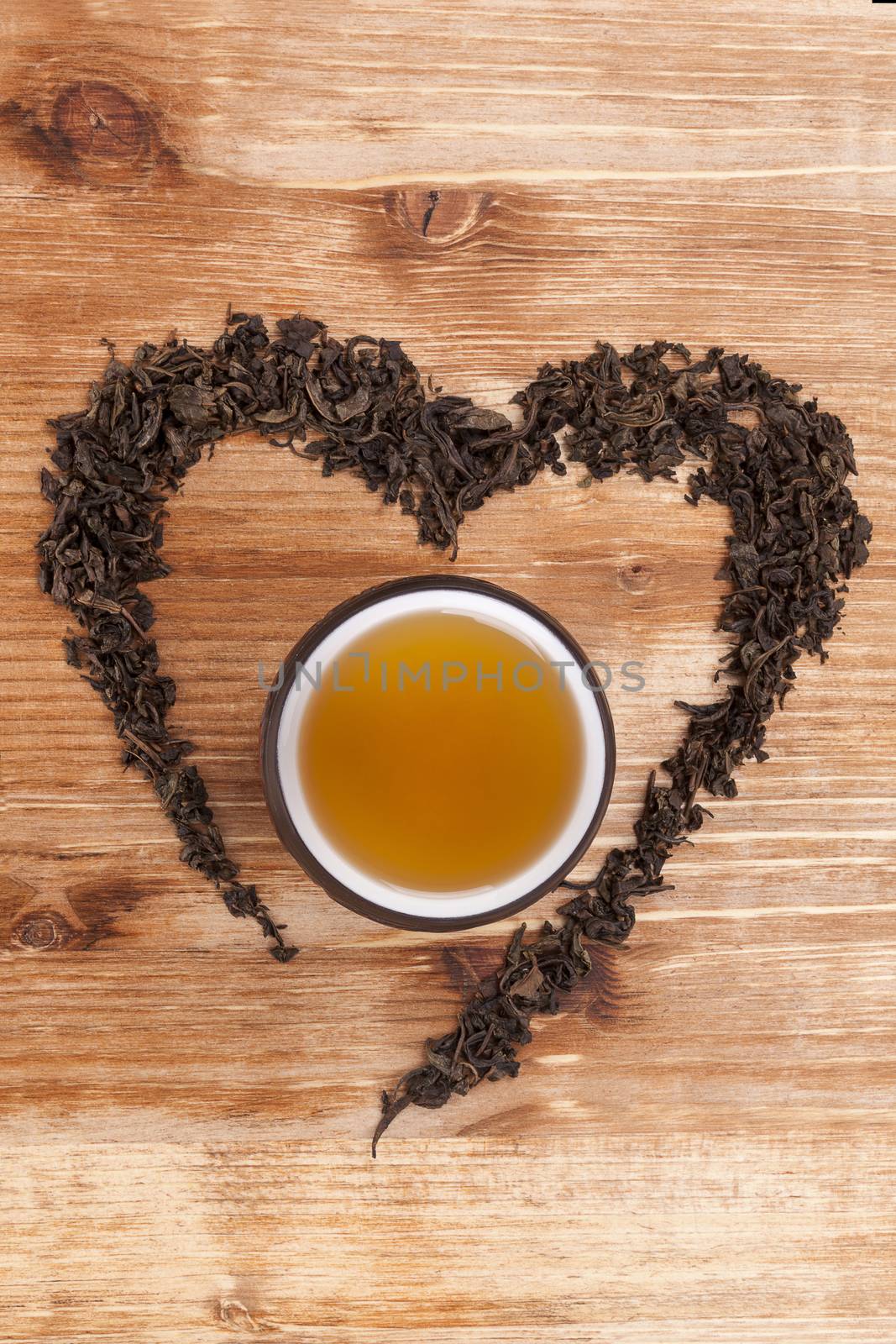 Green tea leaves in heart shape with cup of tea on wooden background. I love tea concept.