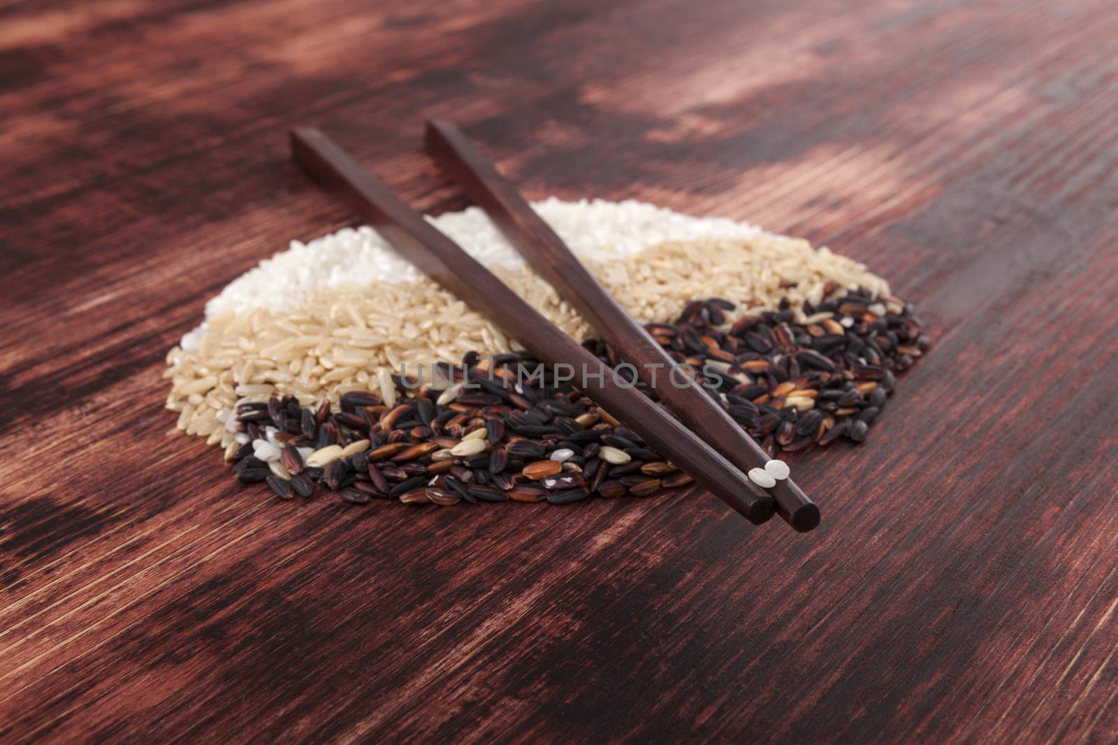 White, natural and wilde rice with chopsticks on dark wooden background. Healthy rice cooking concept.