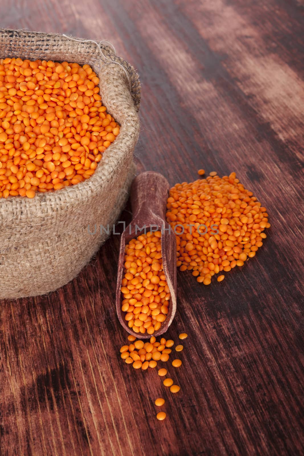 Red lentils in brown burlap sack with wooden spoon on dark wooden background. Healthy eating.