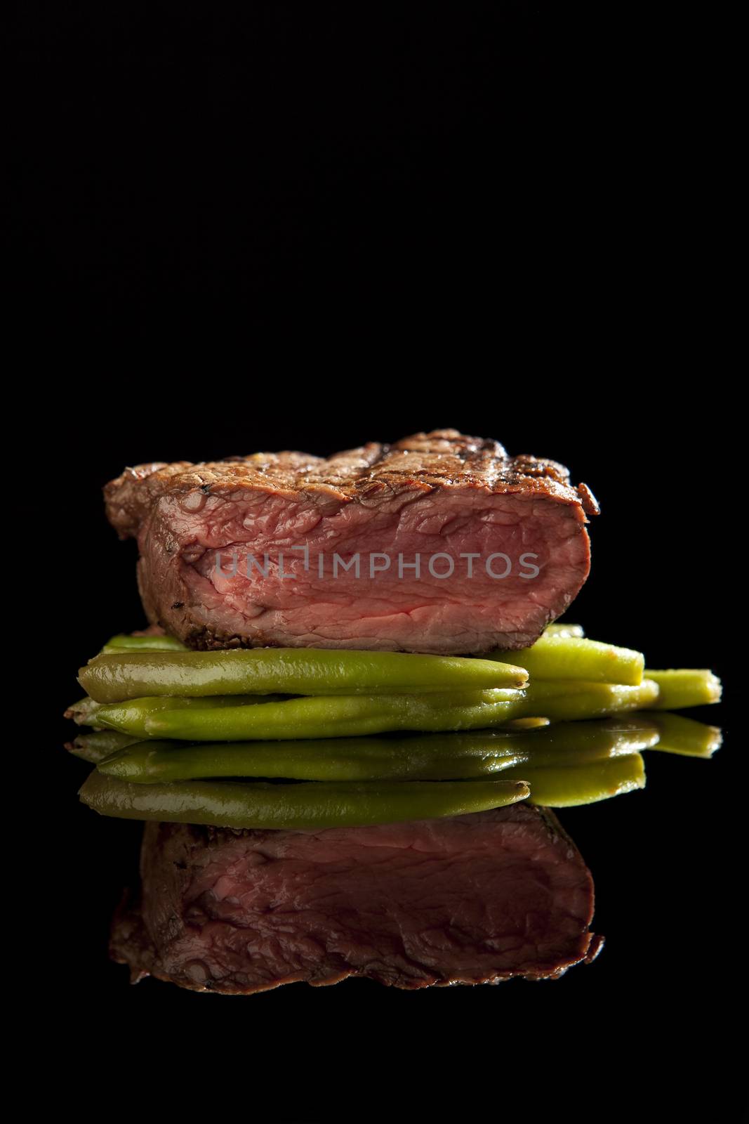 medium rare beef steak with beans on black background