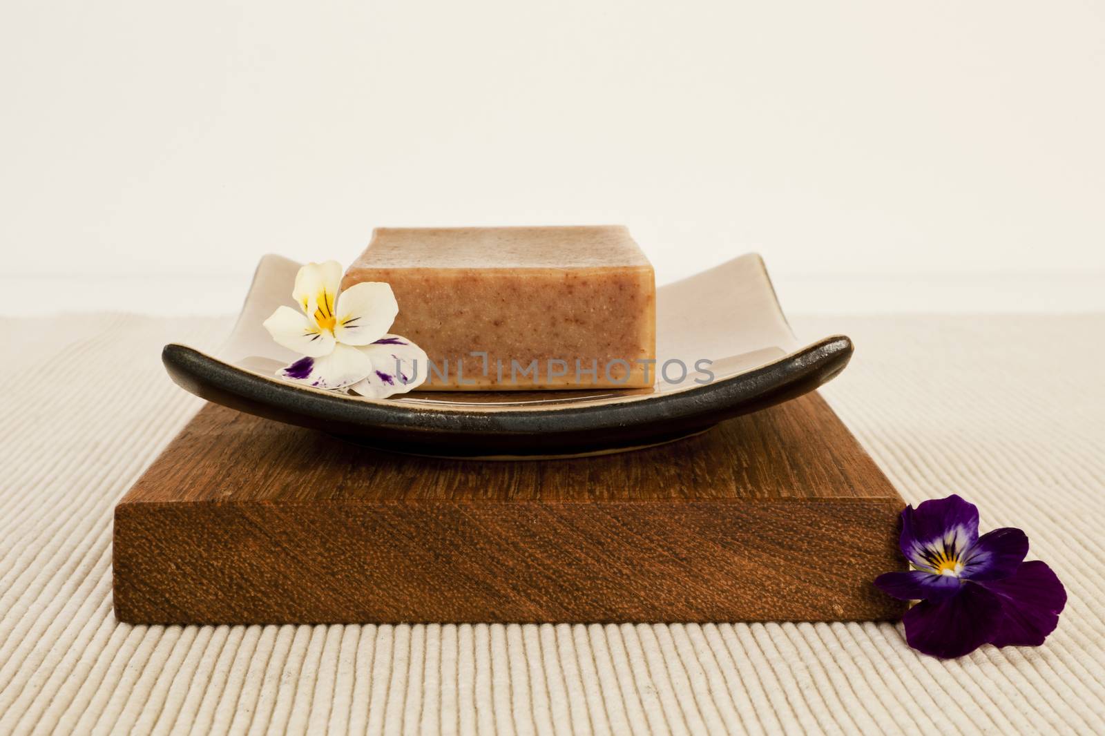 Spa still life with organic soap bar, flower blossom on a beautifull ceramics plate on wood.