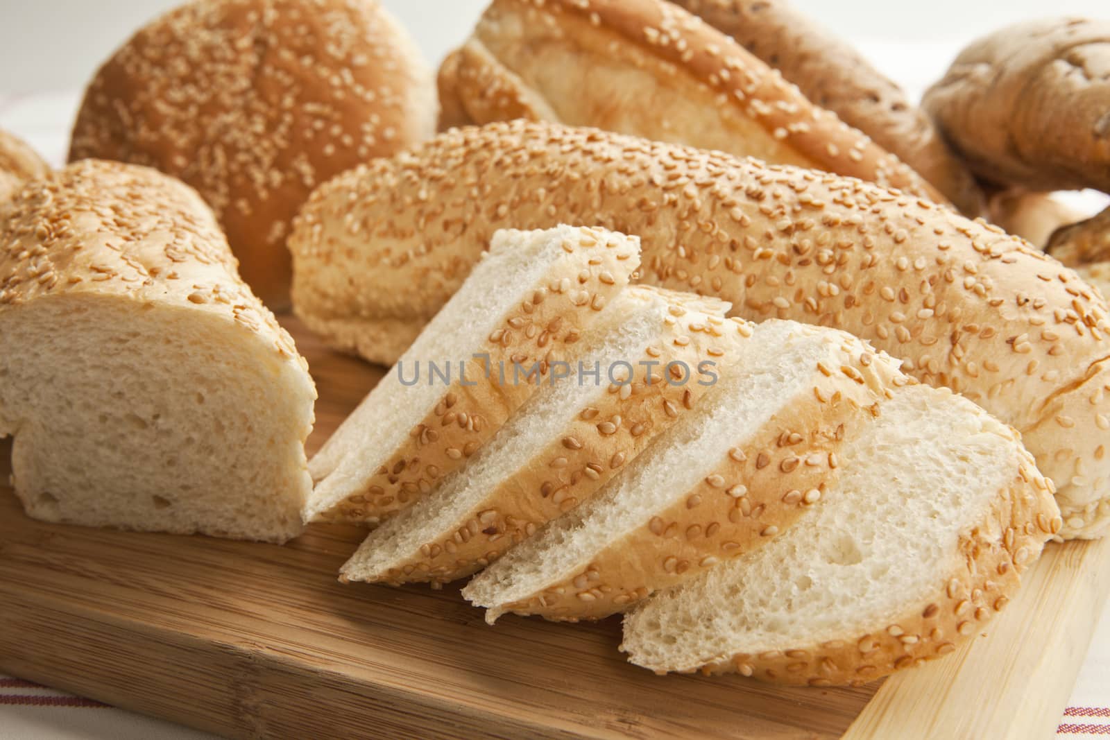 Sliced white sesame baguette on wooden slab.