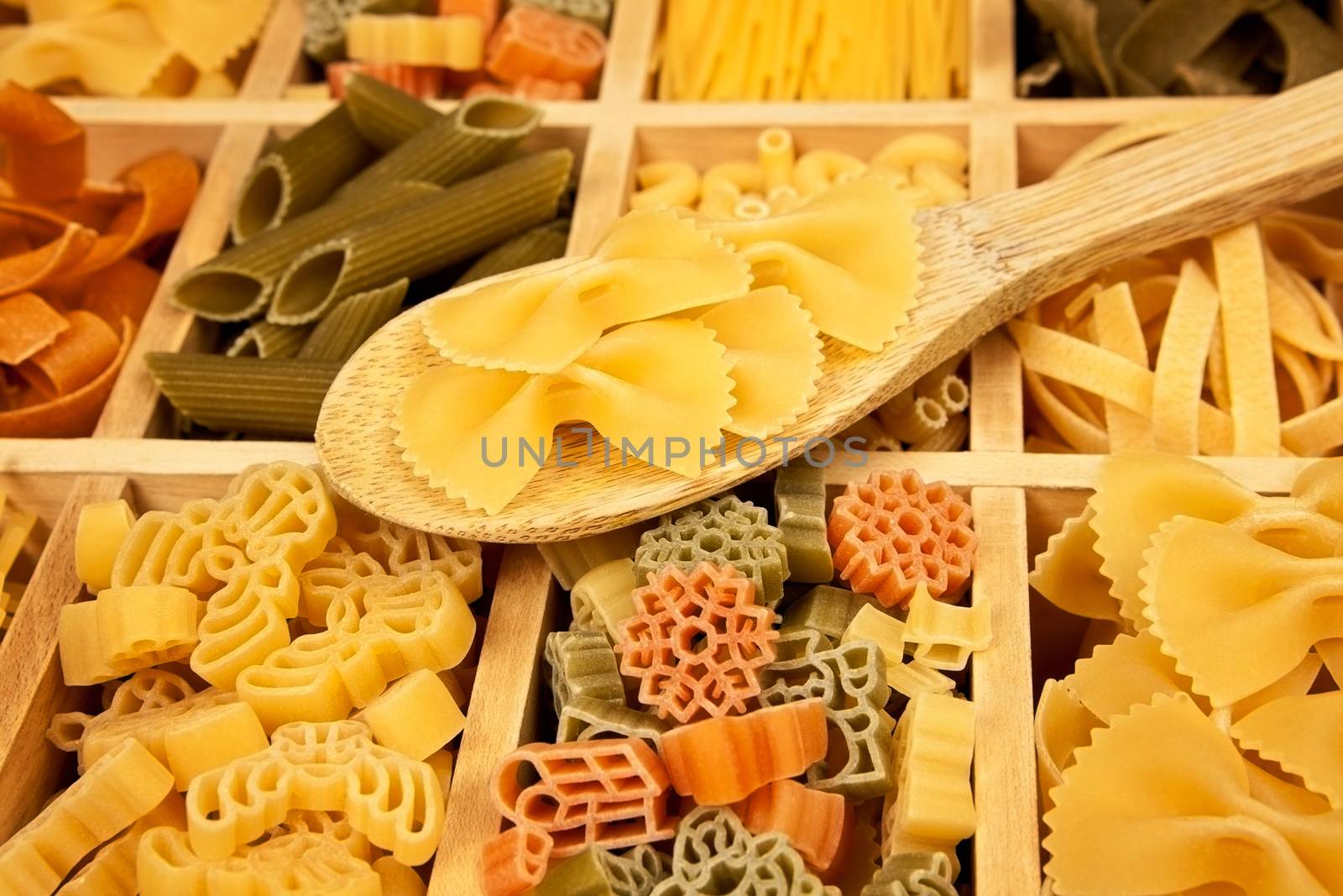 Different pasta sorts arranged in wooden box with wooden spoon.