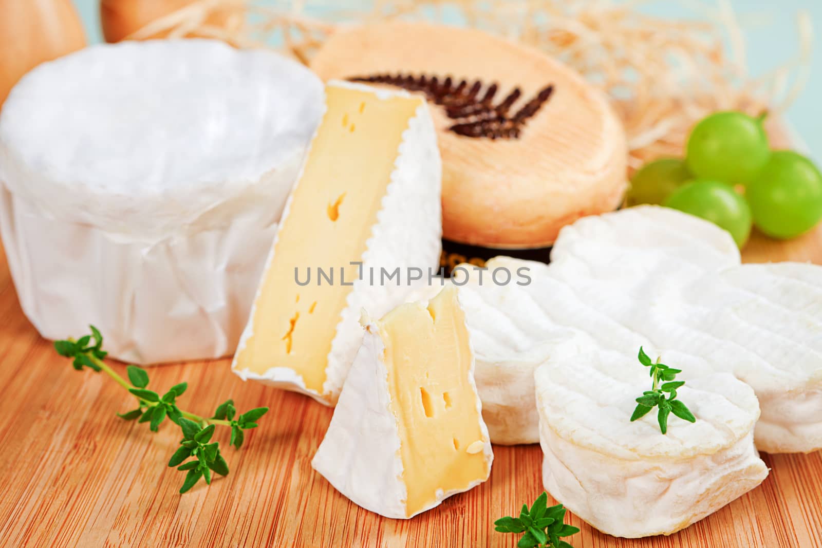 Luxurious cheese variation arranged on wooden board with fresh herbs and grapes.