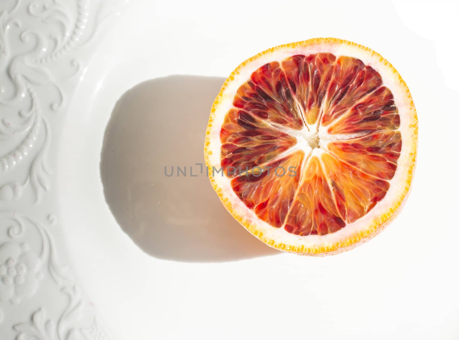 Red orange sliced with shadow on white plate with patterned edge.