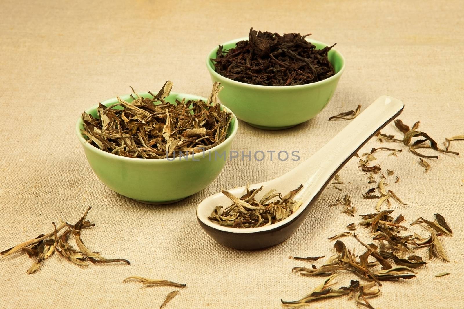 Dry green tea and black tea leaves arranged on brown background.